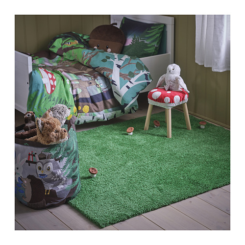 Habitación infantil con alfombra verde SKOGSDUVA, materiales 100% reciclados. La alfombra cubre el suelo, rodeada de juguetes y cama. Superficie suave y amigable para el juego.