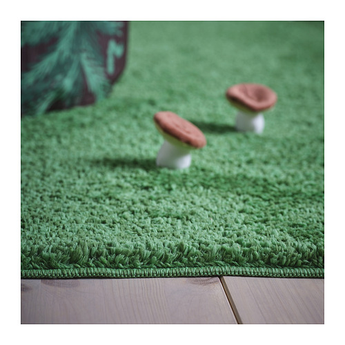 La alfombra verde suave y afelpada imita la hierba del bosque. Dos hongos de juguete se sientan encima, de textura vívida.