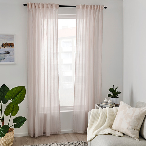 Sala de estar luminosa con una gran ventana blanca, cortinas BYMOTT beige transparentes, acogedor sofá crema con almohadas y plantas verdes. Obras de arte en la pared.