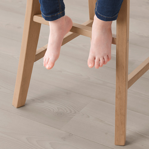 Pies de niño en jeans que cuelgan de una silla junior de madera, brindando un soporte cómodo.