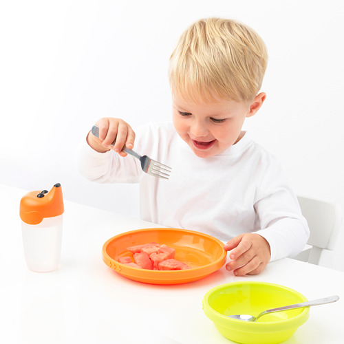 El niño come de un tazón de naranja con un tenedor de acero inoxidable. Apto para lavavajillas, edad 3+. Brillante, divertido, apto para niños.