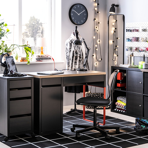 Moderna oficina en casa con escritorio MICKE negro, silla roja, reloj, planta y guirnalda de luces.