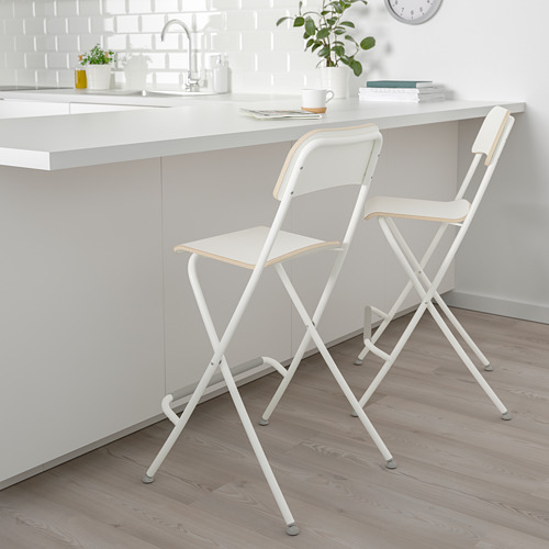 Dos taburetes FRANKLIN plegados debajo de una elegante encimera de cocina con tazas y plantas.