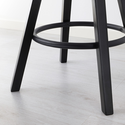 Taburete de metal negro con reposapiés circular y regulable en altura, sobre suelo de madera clara. Los materiales de alta calidad garantizan estabilidad y durabilidad.