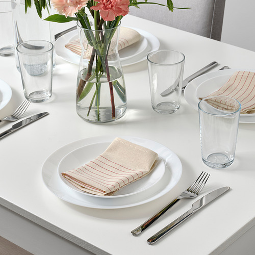Mesa con platos blancos, servilletas a rayas dobladas, vasos, cubiertos y un jarrón con flores, dispuestos ordenadamente sobre una mesa blanca.