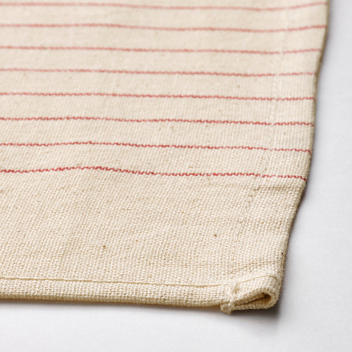 Servilleta de algodón beige doblada con rayas rojas sobre superficie gris.
