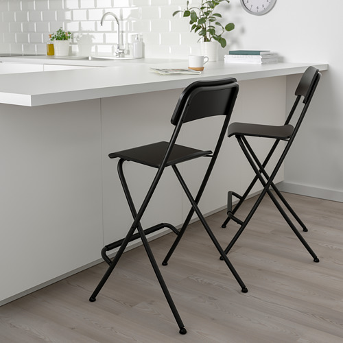 Dos taburetes de bar FRANKLIN negros junto a una isla de cocina blanca con planta, taza y reloj.