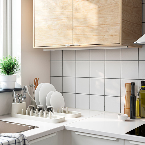 Cocina moderna con armarios de madera, encimeras blancas, escurridor de platos STÄMLING, plantas, botellas de aceite.