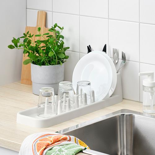 Fregadero de cocina con escurridor de platos STÄMLING que sostiene platos, vasos y cubiertos, junto a un dispensador de plantas y jabón.