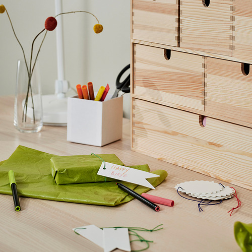 Espacio de trabajo organizado con cajones de madera, regalo de cumpleaños, bolígrafos, marcadores, recortes de papel y un jarrón con flores.