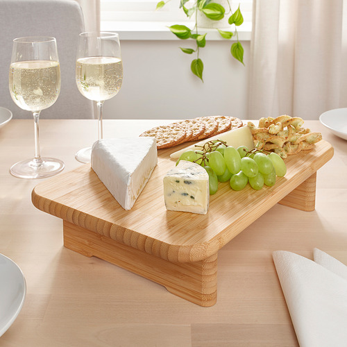 Tabla de servir de madera con quesos, uvas y galletas; Una copa de vino.