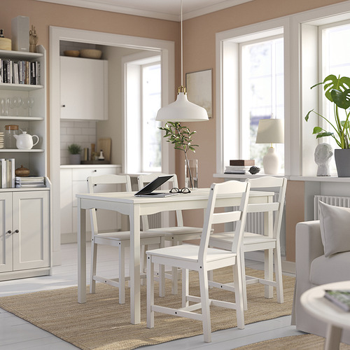 Comedor luminoso y minimalista con mesa y sillas HAUGA blancas, alfombra de yute, grandes ventanales, planta verde, lámpara colgante blanca y estantería.