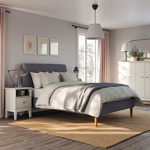 Un acogedor dormitorio con una cama tapizada IDANÄS gris, suelos de madera clara y una gran ventana.
