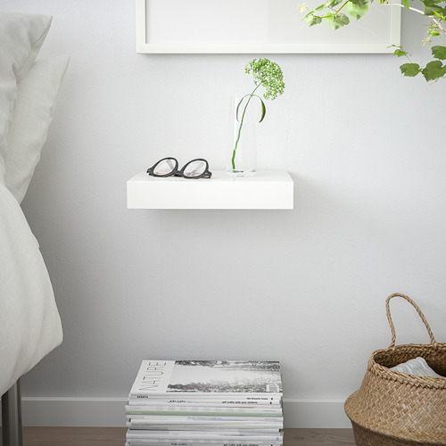 Estantería blanca LACK con vasos, jarrón y vegetación, además de revistas y pañuelos de papel. Espacio neutro y organizado.