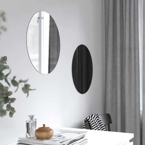 Dos espejos ovalados en la pared; uno reflectante, otro negro, encima de la mesa con elementos decorativos.