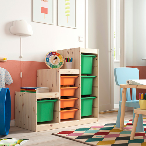 Almacenamiento TROFAST: madera clara, cajas verdes y naranjas, grandes, coloridas, con varios compartimentos. Mueble alto con silla azul, espacio de juego.