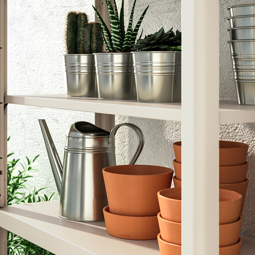 Estantería con regadera de plata y macetas de terracota, apta para uso en interiores o exteriores.