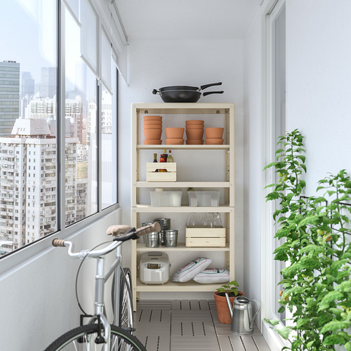 Balcón con mueble de almacenamiento KOLBJÖRN blanco con ollas, sartenes y utensilios de cocina. Una bicicleta y una planta al lado, con vista a la ciudad desde la ventana.