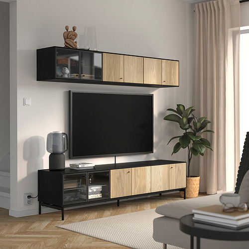 Sala de estar moderna con banco y estante de televisión BOASTAD, pared gris claro, cortinas beige, planta en maceta y muebles grises.