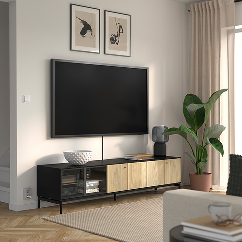 Sala de estar moderna con mueble de TV negro BOASTAD, plantas, arte, cuenco blanco, libros apilados. Cortina beige, sofá blanco, suelo de madera.