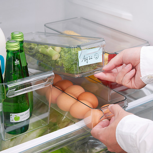 La persona organiza el refrigerador con cajas de almacenamiento transparentes y apilables. Etiquetas en las cajas para una fácil identificación.
