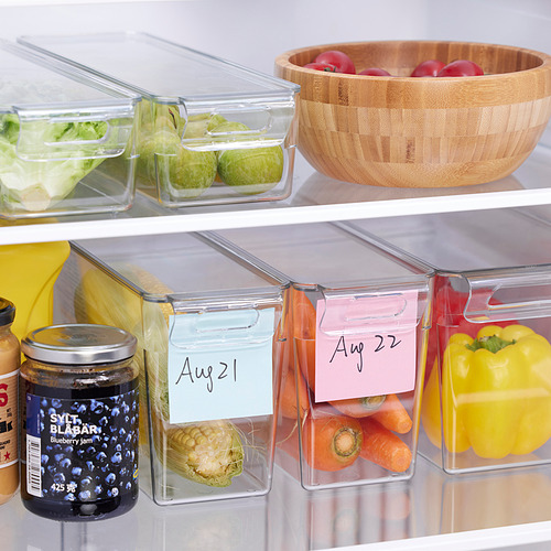 Nevera con verduras organizadas en recipientes apilables con etiquetas de fecha.