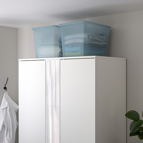 Dos cajas RYKTA de plástico transparente azul claro sobre un armario blanco, más grandes que una camisa blanca cercana.