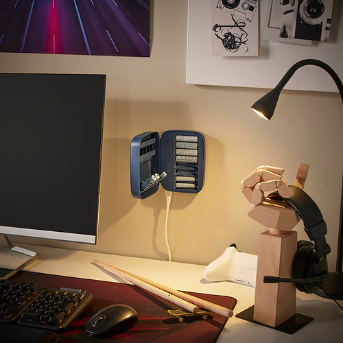 Moderno espacio de trabajo con cargador LITOSFÄR, monitor, teclado, ratón, monopatín, auriculares y estatua de madera.