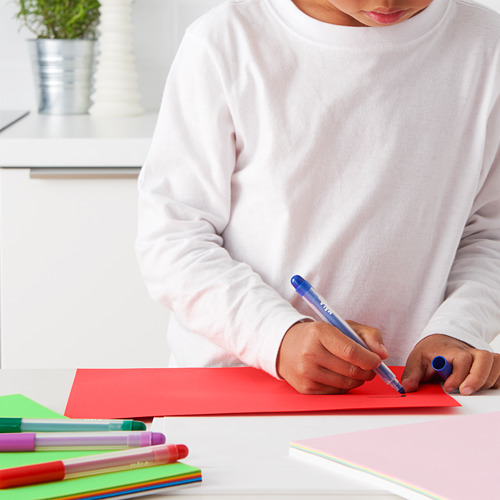 Un niño con un suéter blanco dibuja con un bolígrafo azul sobre papel rojo. Varios bolígrafos de colores están cerca.