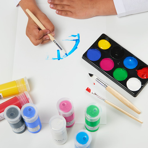 Manos de niños pintando con pintura al agua MÅLA. Colores vivos en tubos y bandeja, con pinceles, sobre papel blanco.