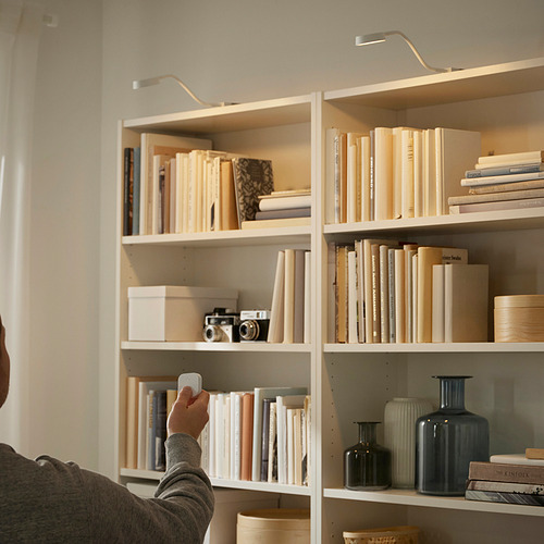 Persona ajustando la lámpara regulable sobre una estantería blanca, iluminando libros y decoración.