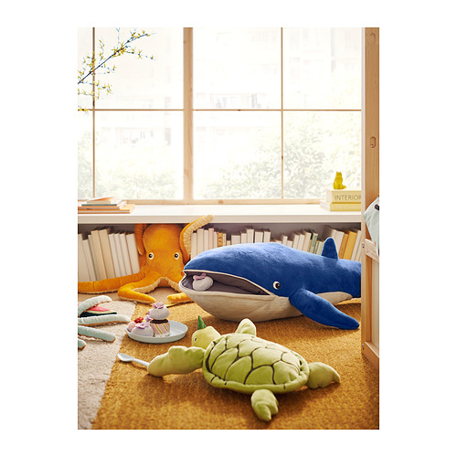 Acogedora habitación con criaturas marinas de felpa: ballena azul, pulpo naranja, tortuga verde. Peluches sobre alfombra amarilla junto a la ventana.