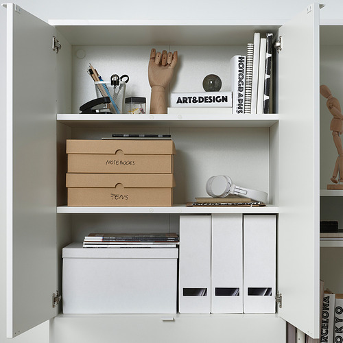 Armario blanco con arte, libros de diseño y cajas VATTENTRÅG para notas y bolígrafos, organizados de forma ordenada.