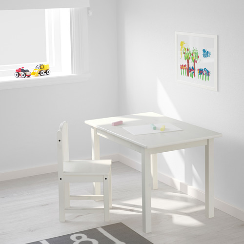 Los niños juegan con mesa y silla blancas, perfectas para rompecabezas y dibujos. Ubicado cerca de una ventana con una decoración colorida.