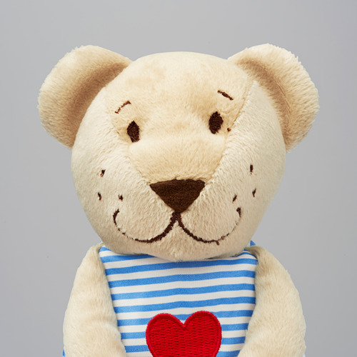 Osito de peluche beige con dulce, bordado con un babero de rayas azules y blancas con un corazón rojo.