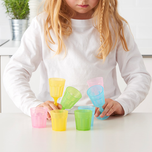 La niña juega con tazas y vasos de colores, apilando, imaginando.