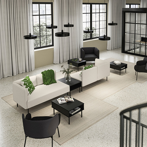 Sala de estar moderna con sofá LILLEHEM, detalles en verde, muebles negros, grandes ventanales.