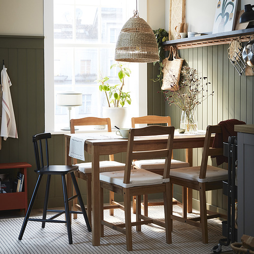 Acogedora zona de comedor con juego de madera HÄGERNÄS, gran lámpara colgante, planta y estantes decorados.