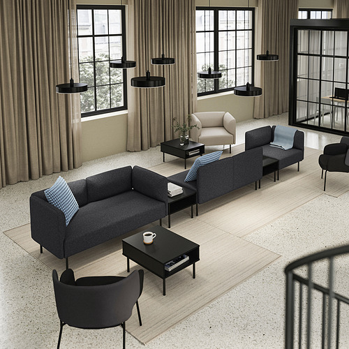 Salón moderno con sofá modular LILLEHEM en color gris, mesas de centro negras, lámparas colgantes negras y grandes ventanales con cortinas beige.