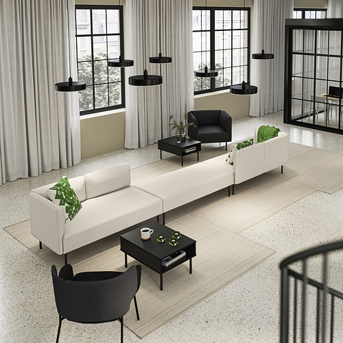 Moderno salón con mesas TUNSTA, sillón negro, sofás, lámparas colgantes, grandes ventanales, almohadas verdes.