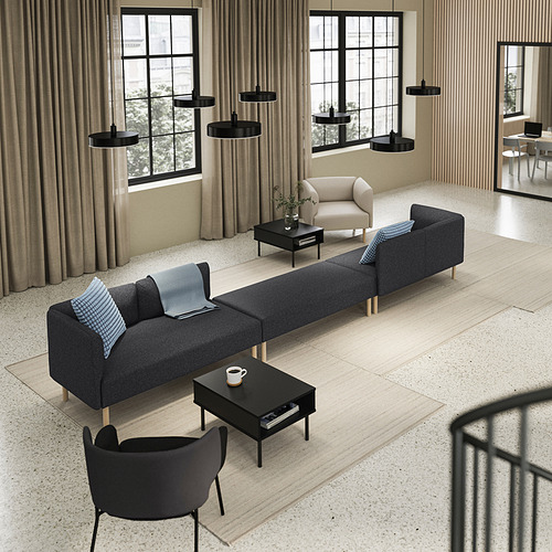 Un espacio de vida moderno con un sofá modular gris LILLEHEM y una mesa de centro negra, acentuada con almohadas azules.