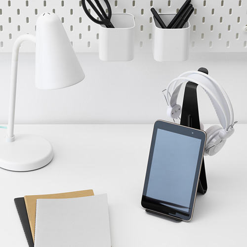 Escritorio con soporte para tableta que sostiene teléfono y auriculares, lámpara, papeles y contenedores de almacenamiento.
