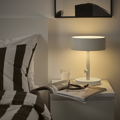 Dormitorio moderno con lámpara NYMÅNE, almohadas a rayas, libro y vaso de agua.