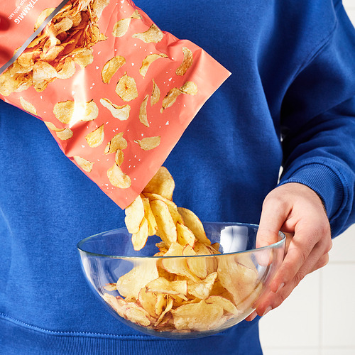 Persona que vierte patatas fritas rústicas del paquete rojo en un tazón transparente.