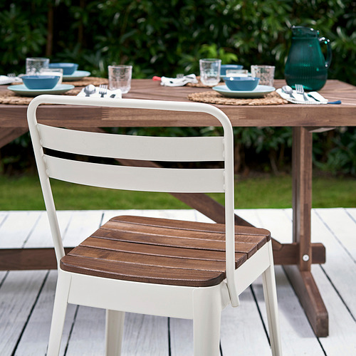 Silla de exterior de metal blanco y madera en mesa de jardín con platos azules y jarra de vidrio verde.