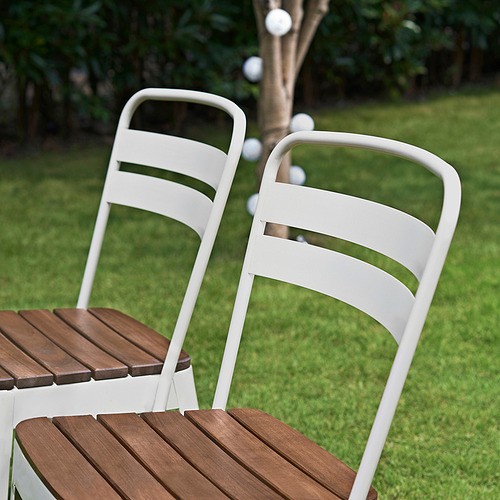 Dos sillas metálicas NORRMANSÖ blancas con asientos de madera en el exterior. Ideal para comer, ligero, resistente, con respaldos curvos.