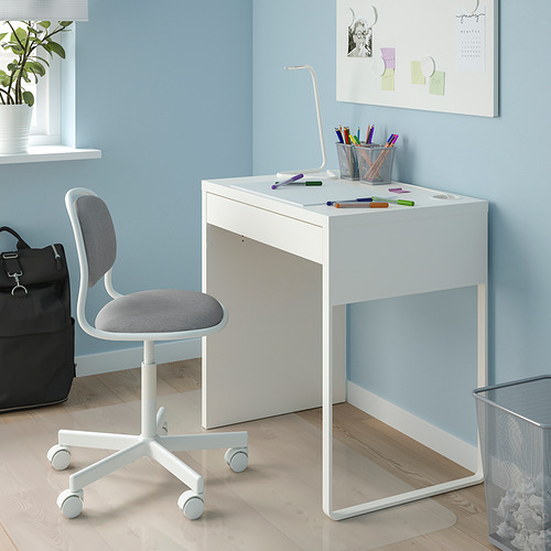 Configuración de oficina en casa blanca: escritorio pequeño, silla giratoria, bolígrafos de colores, lámpara. Pared azul, suelo de madera clara. Compacto y funcional.