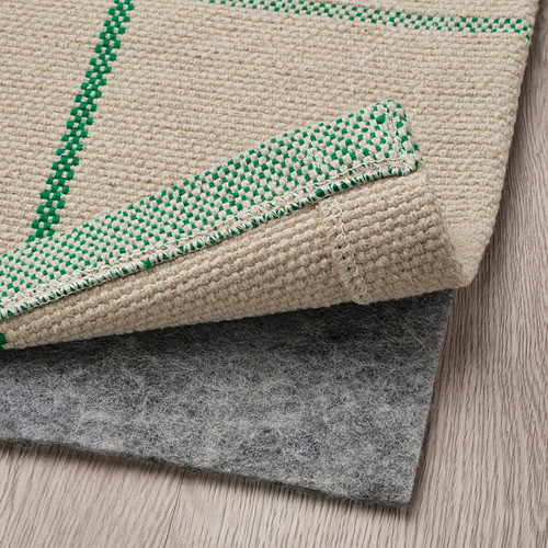 Una alfombra crema con cuadros verdes colocada sobre una parte inferior de fieltro gris, ideal para las zonas de comedor.
