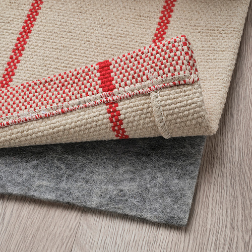 Alfombra de rayas rojas y beige doblada, subsuelo a la vista, que muestra su uso y diseño.