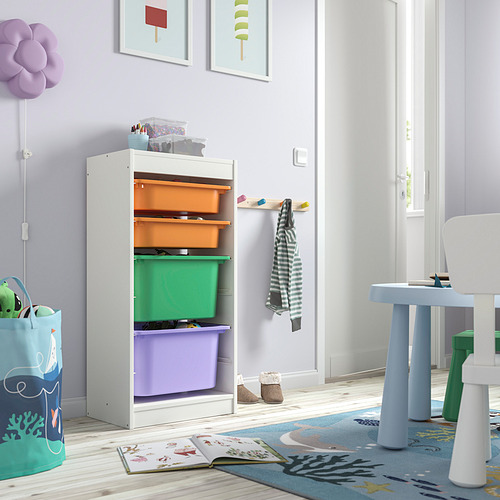 Mueble de almacenaje TROFAST blanco con cubos de colores. Fácil acceso para los niños, se adapta a juguetes y libros. Contenedores morados, verdes, naranjas. Pequeña zona de juegos cercana.